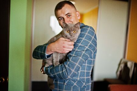 Handsome groom posing with a little cute kitten in his room.の写真素材