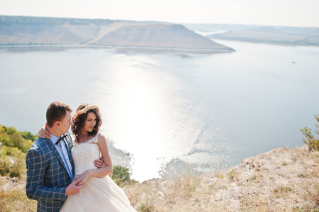 Pretty bride and groom kissing on the edge of rocky cliff with a stunning scenery on the background.の写真素材