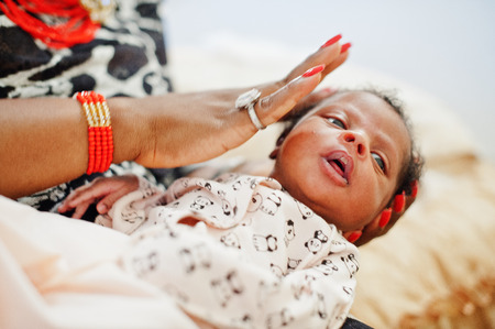 Beautiful black woman in ethnic clothing holding little baby.の写真素材