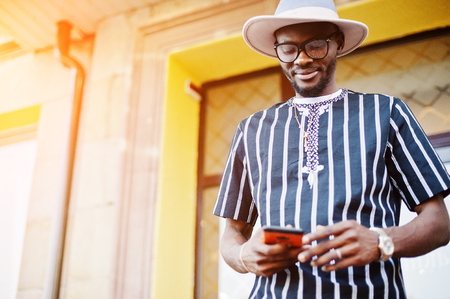 Attractive african american man in striped shirt, hat and sunglasses walking on the street in the downtown.の写真素材