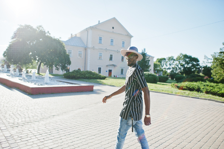 Attractive african american man in striped shirt, hat and sunglasses walking on the street in the downtown.の写真素材