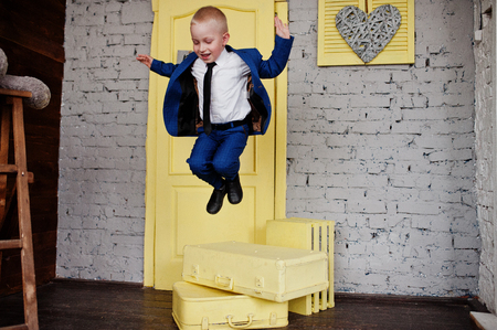 Portrait of a small cute boy jumping off the yellow boxes  in the official clothing in the studio with andbright doors.の写真素材