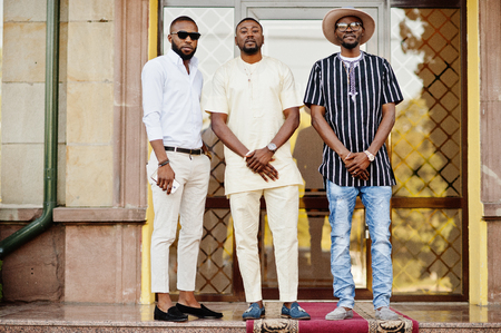 Black men stylishly clothed standing and talking outside on the street in the downtown.