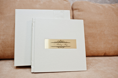 Sohisticated white leather wedding photobook or photo album with golden inscription standing on the sofa.の写真素材