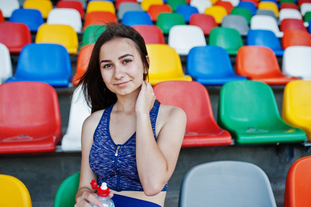 Portrait of a pretty woman in sportswear sitting and drinking water in the stadium.の写真素材