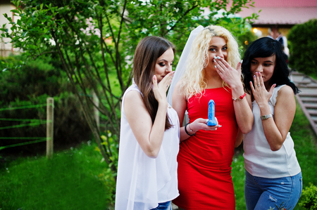 Beautiful bride in red dress showing a soap in penis shape to her bridesmaids at bachelorette party.の写真素材