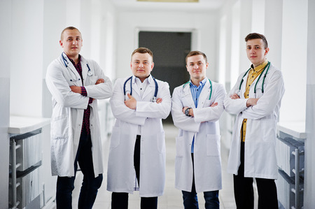 Four confident male doctors in white coats with stethoscopes standing in the hallway in hospital.の写真素材