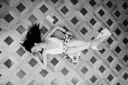 Portrait of a stunning young woman in gorgeous dress laying on the floor with her smartphone. Black and white photo.の写真素材