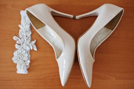 Bridal high-heeled shoes on the wooden surface and wedding bandage beside them.の写真素材