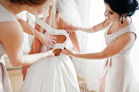 Bridesmaids helping gorgeous bride to dress up and get ready for her wedding ceremony.の写真素材