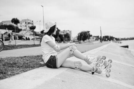 Portrait of a gorgeous young woman in casual clothes and cap sitting on the ground next to the lake. Black and white photo.の写真素材