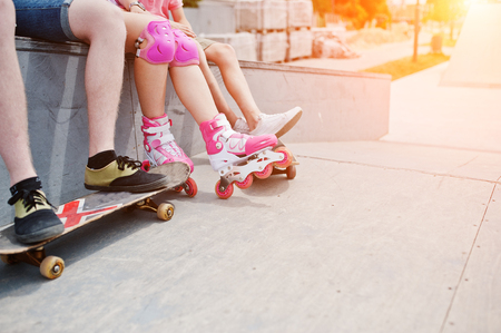 Close-up photo of male legs on skateboard and female legs in rollerblades and protection.の写真素材