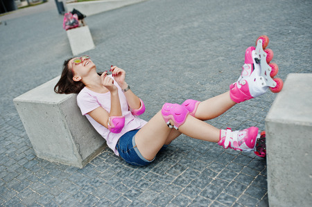 Portrait of a beautiful woman sitting on the ground next to concrete cube wearing rollerblades and...