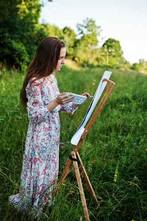 Portrait of an attractive young woman in long dress painting with watercolor in nature.の写真素材