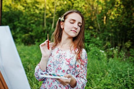 Portrait of an attractive young woman in long dress painting with watercolor in nature.の写真素材