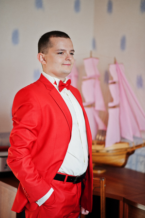 Handsome groom in red tuxedo posing in his room on a wedding day.の写真素材