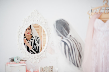 Portrait of a gorgeous bride looking in the mirror and putting on her wedding earrings.の写真素材