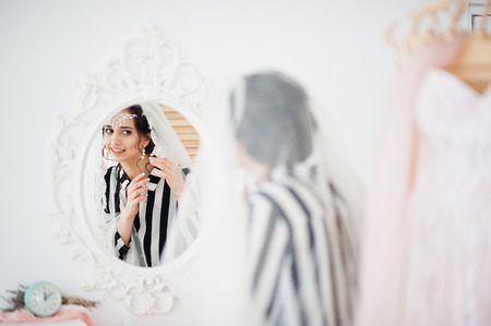 Portrait of a gorgeous bride looking in the mirror and putting on her wedding earrings.の写真素材