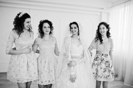 Fantastic bride posing in wedding dress with helpful pretty bridesmaids in big white room. Black and white photo.の写真素材