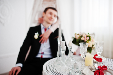 Attractive bride standing next to the groom while he is sitting on the chair at a table.の写真素材