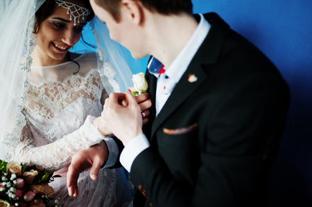 Fabulous wedding couple sitting against blue wall with triangular frames on it in the studio.の写真素材
