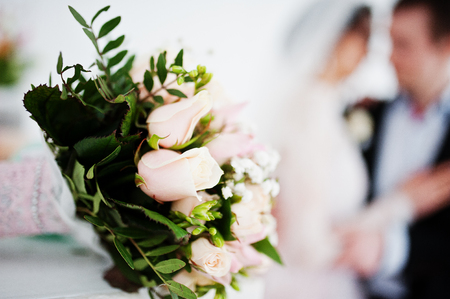 Close-up photo of a bouquet made out of roses laying on the table. Wedding couple in the background.の写真素材