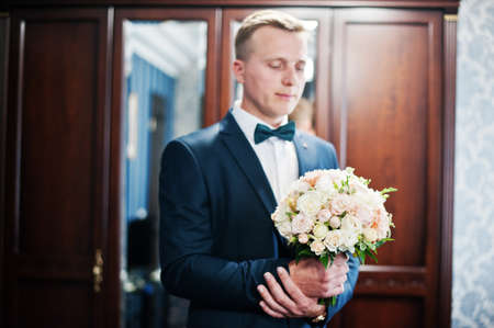 Portrait of a handsome groom posing with bridal bouquet in his cool room on the wedding day.の写真素材