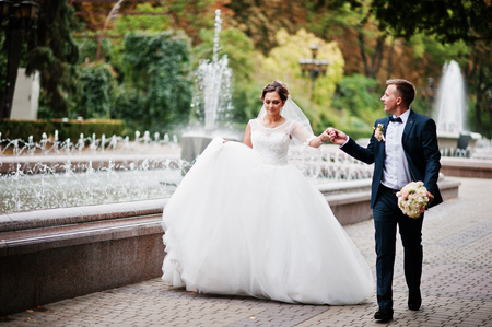 Wedding couple walking and smiling on pavement with a fountain in the background.の写真素材
