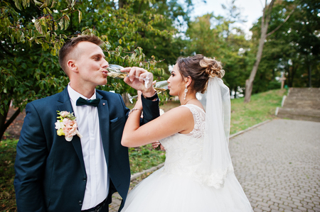 Happy newlyweds drinking champagne outdoor in the park on a wedding day.の写真素材