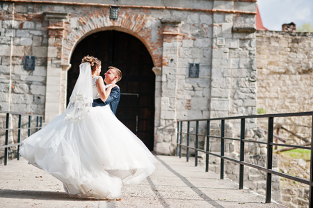 Handsome groom spinning his wife on his hands next to the old gates.の写真素材