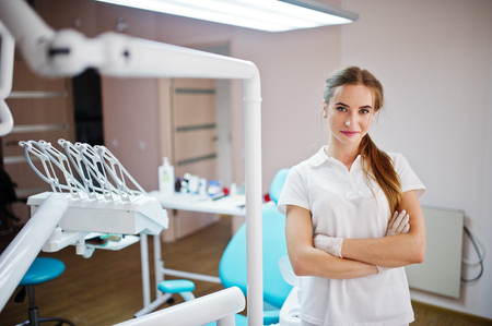 Good-looking female dentist posing in white coat in a modern well-equipped cabinet.の写真素材