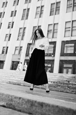 Portrait of a fabulous young successful woman in white blouse and broad black pants posing on the stairs with a huge white building on the background.の写真素材