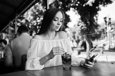 Portrait of an attractive young businesswoman with a mojito cocktail texting a message on her smatphone. Black and white photo.の写真素材