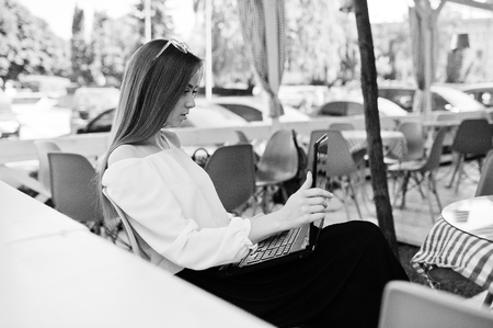 Portrait of a strong independent successful businesswoman wearing smart casual clothing and glasses working on a laptop in a cafe. Black and white photo.の写真素材