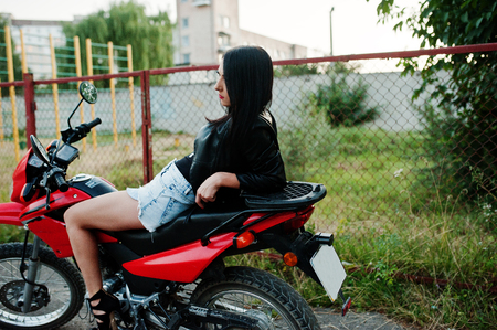 Portrait of a cool and awesome woman in dress and black leather jacket sitting on a cool red motorbike.の写真素材