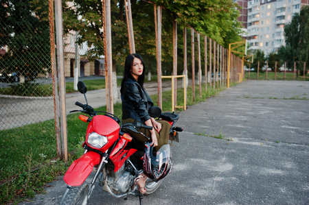 Portrait of a cool and awesome woman in dress and black leather jacket sitting on a cool red motorbike.の写真素材