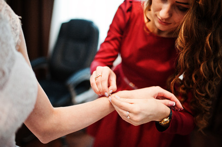 Good-looking bridesmaid helping bride to put a bracelet on.