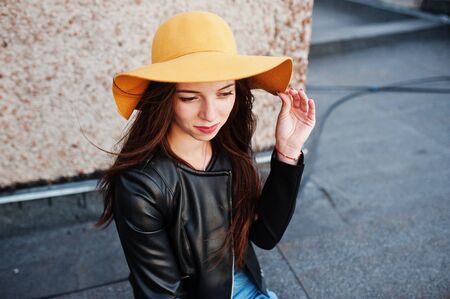 Portrait of a beautiful young woman in black leather jacket and orange hat sitting on a rooftop.の写真素材