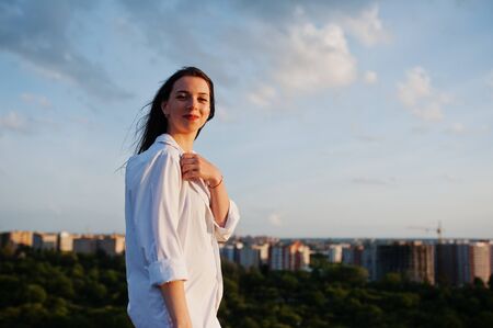 Portrait of an outstanding woman in white male shirt posing on top of the building with charming scenery on the background.の写真素材