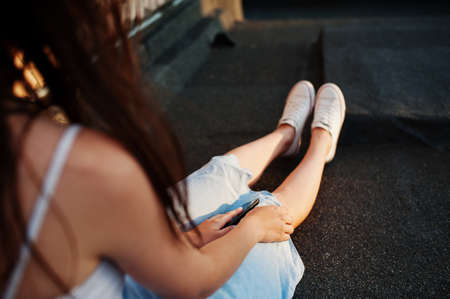 Close-up photo of a woman's hand holding a phone with earphones plugged into it.の写真素材