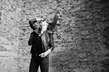 Red haired stylish girl in sunglasses wear in black, against abadoned place with brick walls.の写真素材