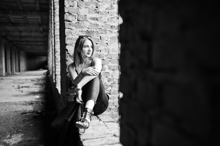 Red haired stylish girl in sunglasses wear in black, against abadoned place with brick walls.の写真素材