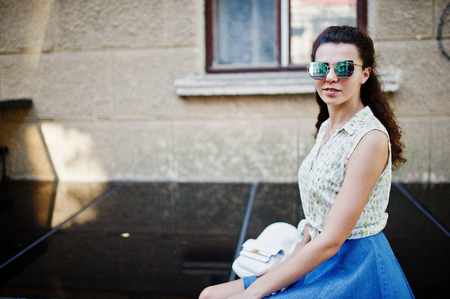 Curly stylish girl wear on blue jeans skirt, blouse and sunglasses. Portrait on streets of city.の写真素材