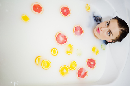 Sexy brunette girl at the bathroom with milk and fruits. Youth bath for body.の写真素材
