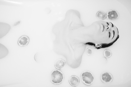 Sexy brunette girl at the bathroom with milk and fruits. Youth bath for body.の写真素材