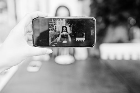 Mobile phone at hand with gorgeous brunette girl sitting on the table in cafe with cup of coffee at...