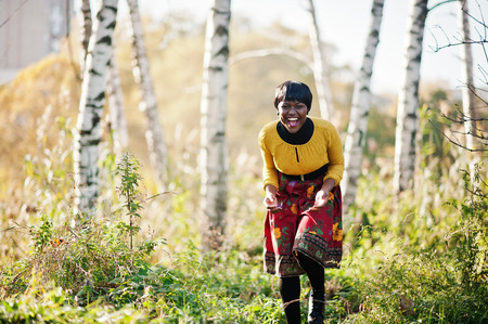 African american girl at yellow and red dress at golden autumn fall park.の写真素材
