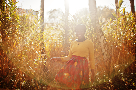 African american girl at yellow and red dress at golden autumn fall park.の写真素材