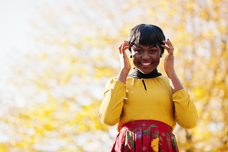African american girl at yellow and red dress at golden autumn fall park.