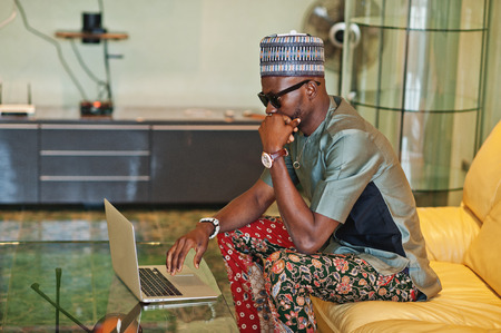 Rich african man sitting on sofa at his appartment and working on notebook.の写真素材